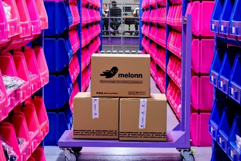 Carro violeta con cajas de cartón Melonn en un pasillo entre estanterías con gavetas rosas y azules
